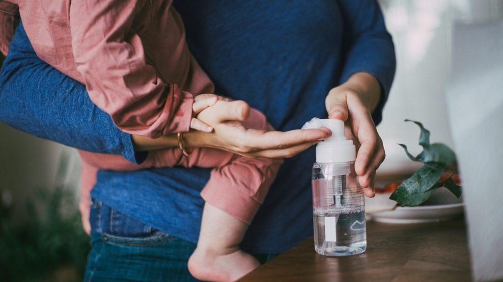 Parent holding a child while using hand sanitizer